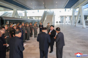 Group of uniformed officials and executives standing in a spacious modern train station, listening to a speaker.