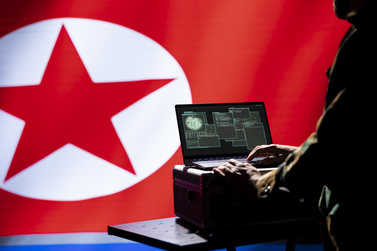 North korea pyongyang regime agent uses military software preventing rockets | nk insider person typing on a laptop at a desk with a large north korea flag in the background