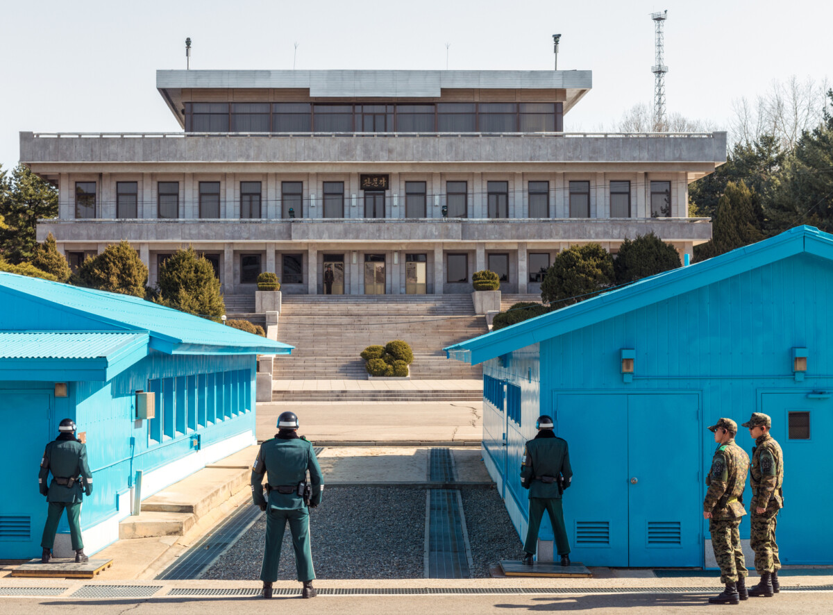 Dmz at the border between north and south korea | nk insider military personnel in green uniforms stand near bright blue temporary buildings with a large concrete government building and steps in the background