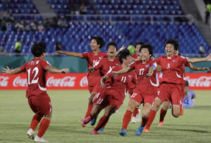 South Korean men's soccer team in red uniforms celebrate together on the field after a goal.