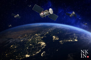 earth viewed from space at night illuminated cities along coastlines with several satellites in orbit and a bright logo in the bottom right corner nkin