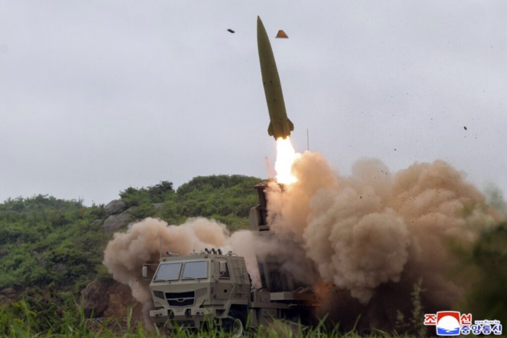 Kju at a missile test site 2 | nk insider mobile missile launcher fires a rocket billowing dust and smoke as the missile lifts off the launch vehicle sits on rough terrain with a forested backdrop