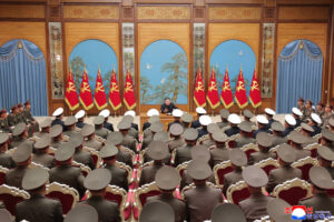 commander giving a speech to a large audience of uniformed soldiers in a grand wood paneled hall with red flags and gold trim