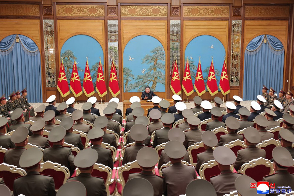 Kju overseeing a military commanders meeting 1 | nk insider commander giving a speech to a large audience of uniformed soldiers in a grand wood paneled hall with red flags and gold trim