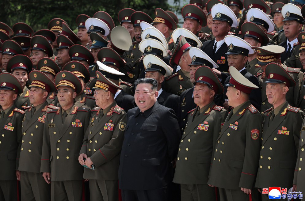 Kju taking a photo with commanders | nk insider kim jong un in a black suit standing among a large group of military officers in green uniforms with caps