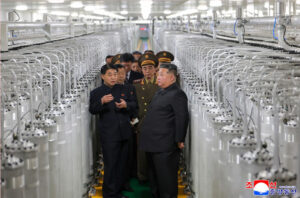 north korean leader kim jong un and officials tour a large textile factory with rows of knitting machines lining the production floor