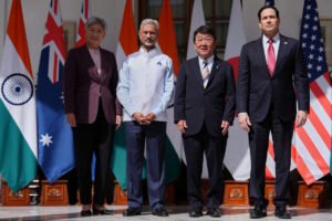 four officials posing for a formal group photo with multiple national flags in the background