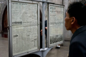 side profile of a man in a suit reading korean newspaper pages mounted in glass display cases outdoors