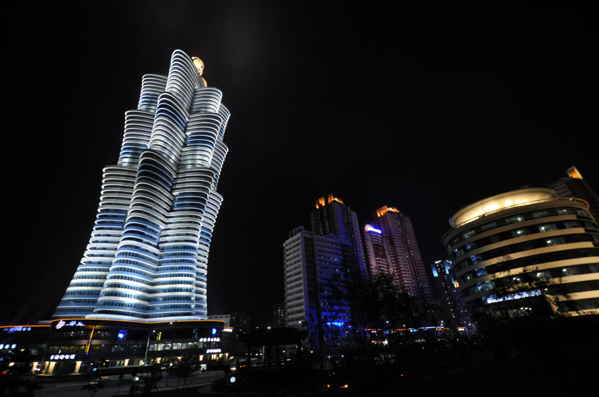 nighttime cityscape with a tall twisting illuminated skyscraper and other lit buildings against a dark sky