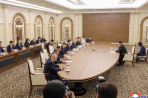 formal diplomatic meeting around a large oval table with officials seated on both sides in a luxurious conference room