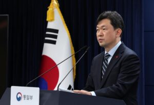 south korean official speaking at a podium with the national flag behind him unification ministry sign visible on the podium