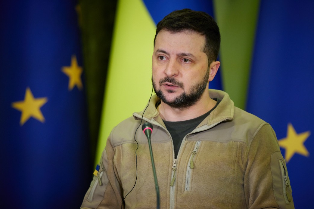 Presidentofukrainevolodymyrzelenskyyinkyivduringtherussoukrainianwar2 | nk insider man in a tan jacket speaks into a microphone with european flags in the background blue with yellow stars and a yellow and blue banner