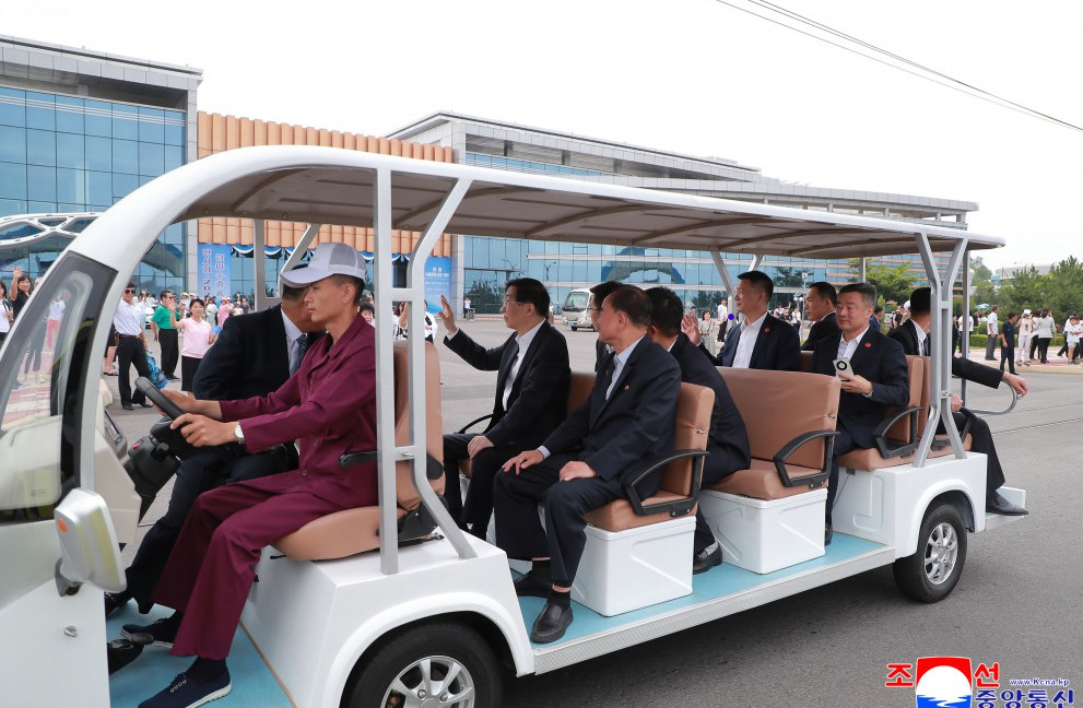 Wansan galma | nk insider group of formally dressed officials riding an open air white shuttle with a driver in burgundy outdoors at a modern building venueleft