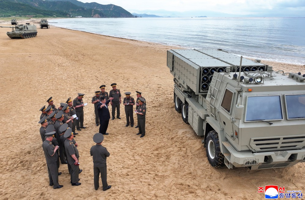 화면 캡처 20260703 203704 | nk insider military briefing on a sandy beach with a large armored vehicle and missile launcher nearby officers in uniform gathered in a circle