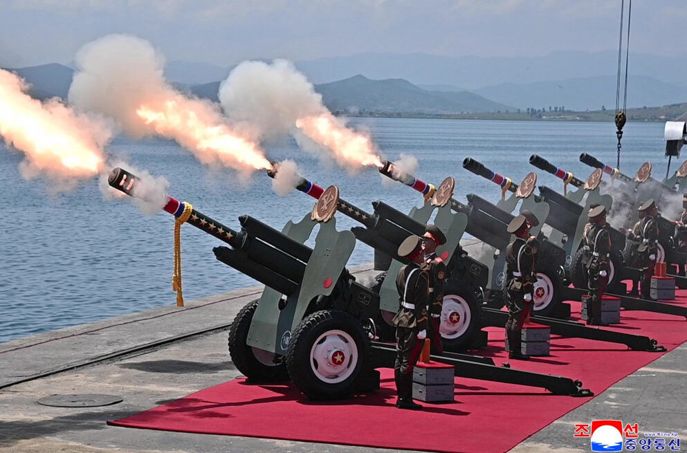 ceremonial artillery battery firing from wheeled cannons on a red carpet by a lake soldiers in dress uniforms