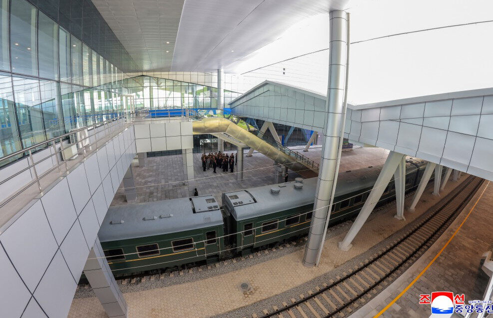 modern train station with a green passenger carriage on tracks beneath a glass and metal canopy a group of people on the platform