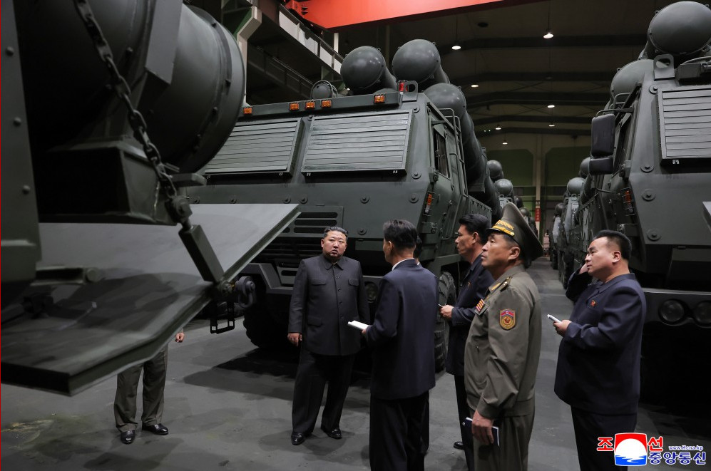2 | nk insider officials in dark suits and a uniformed officer inspect a row of large military armored vehicles inside a hangar