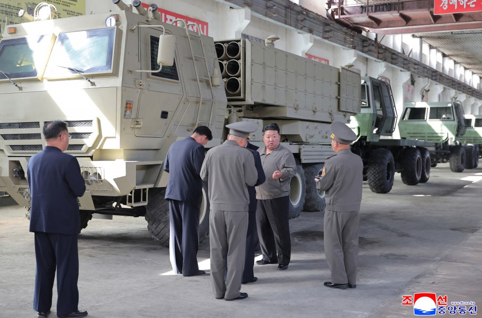 6 | nk insider officials in uniform inspect a large beige military vehicle inside a maintenance yard with more armored trucks in a row behind them