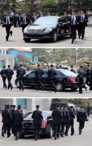 group of suited security personnel escorting a black luxury sedan running in formation around it