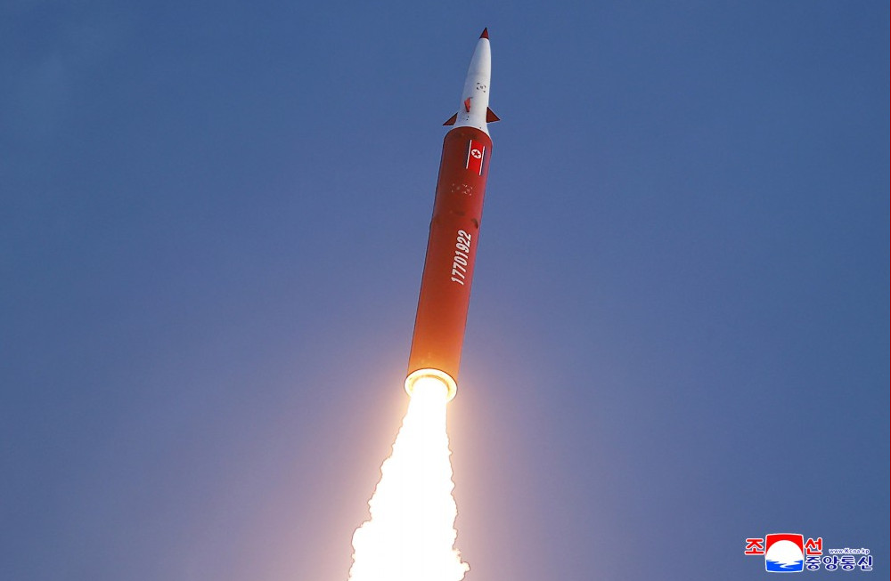Nkmissile | nk insider rocket launching upward orange red booster with white nose cone and bright exhaust plume against a blue sky korean space agency watermark bottom right